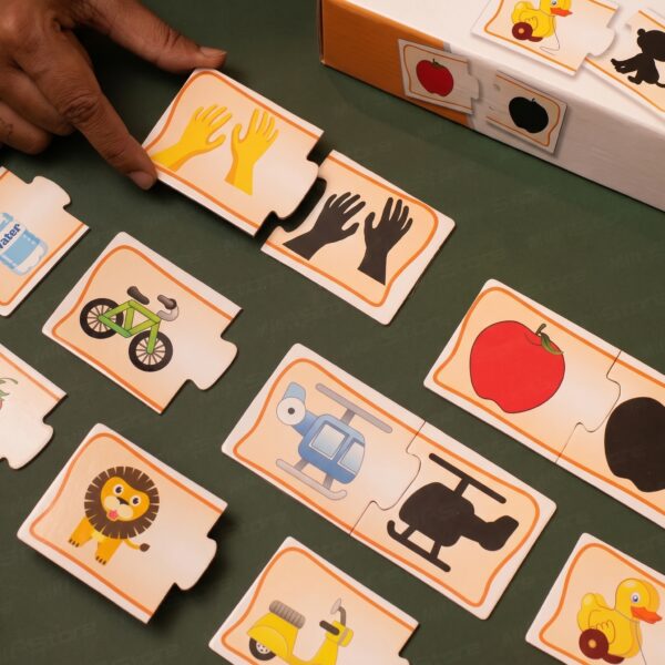 A young boy sitting at a wooden desk, focused on assembling KidNzo Shadow Matching 2-piece puzzles, pairing colorful objects like a frog and helicopter to their silhouettes.